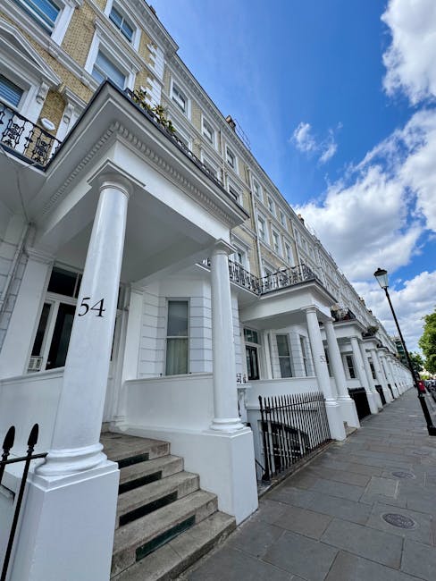 Photograph of a row of elegant white Victorian terraced buildings with ornate architectural details, including decorative moldings, balconies with wrought iron railings, and large sash windows. The fa
