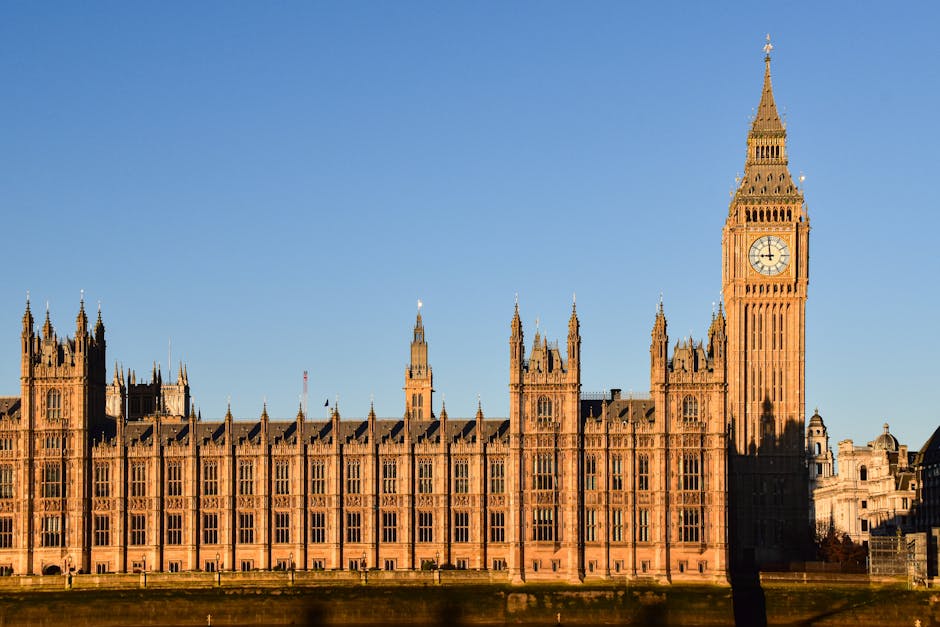 Photograph of the detailed exterior façade of a historic Gothic-style building, likely the Palace of Westminster in London, with numerous pointed arches, ornate stone carvings, and decorative pinnacl
